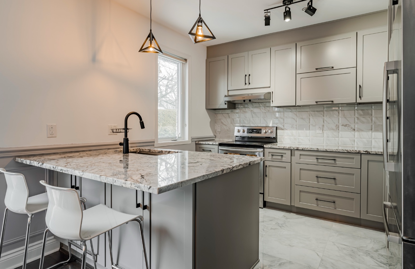 A kitchen with Grey Shaker cabinets, a granite peninsula and a white tile backsplash